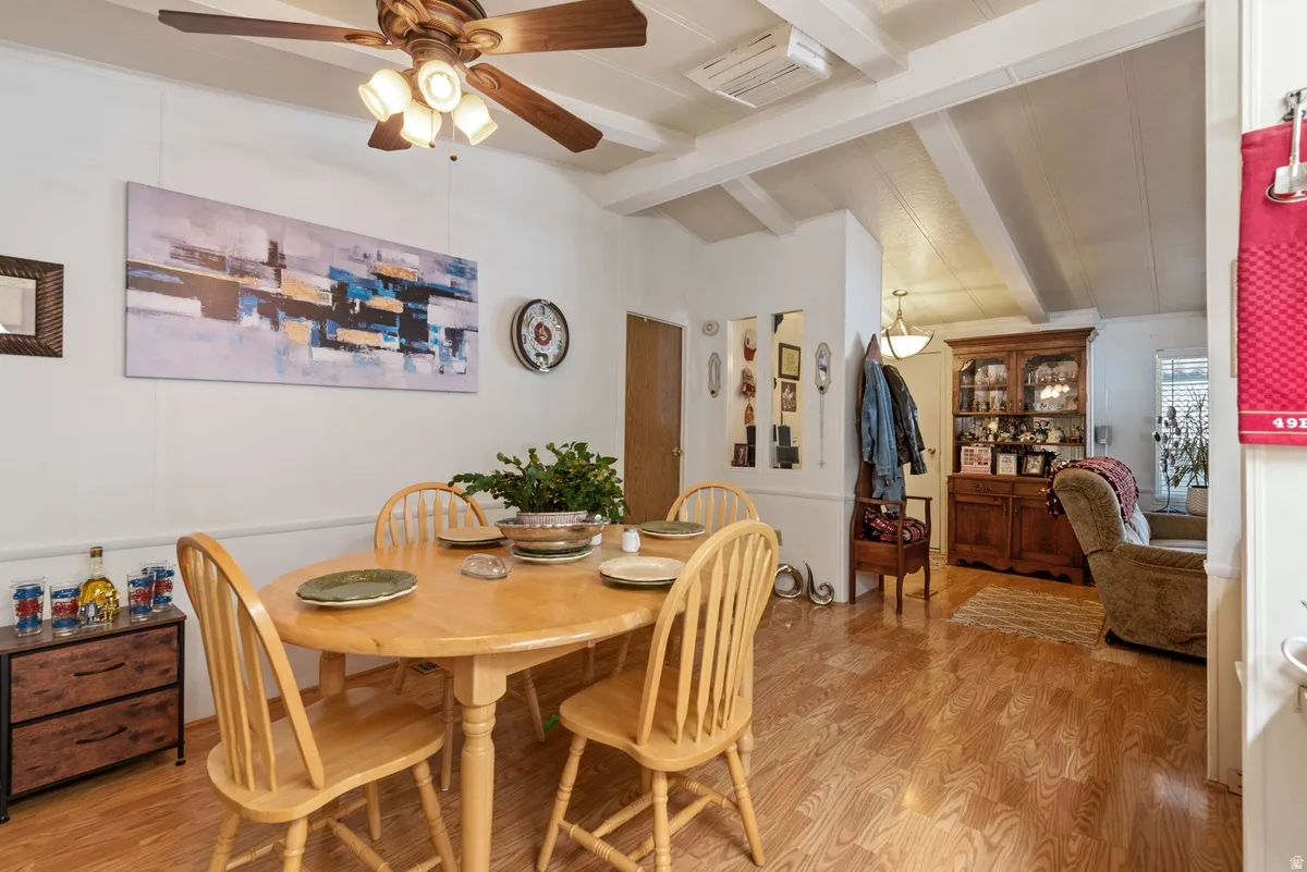 Dining area featuring wood-finish flooring, a ceiling fan with integrated lighting, and exposed ceiling beams