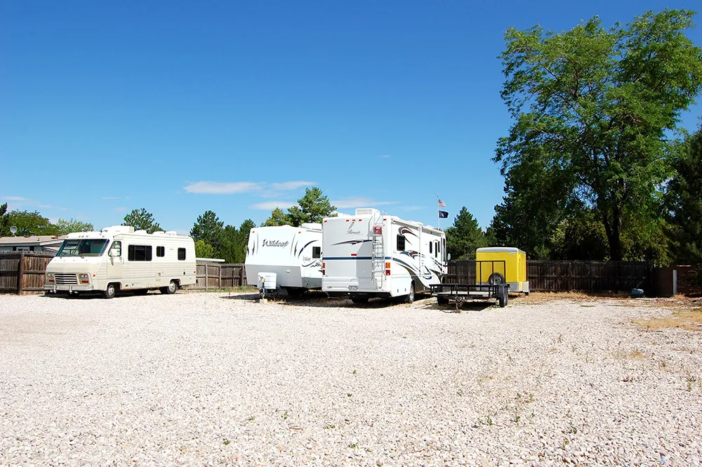 Gravel parking area featuring a privacy fence and mature trees