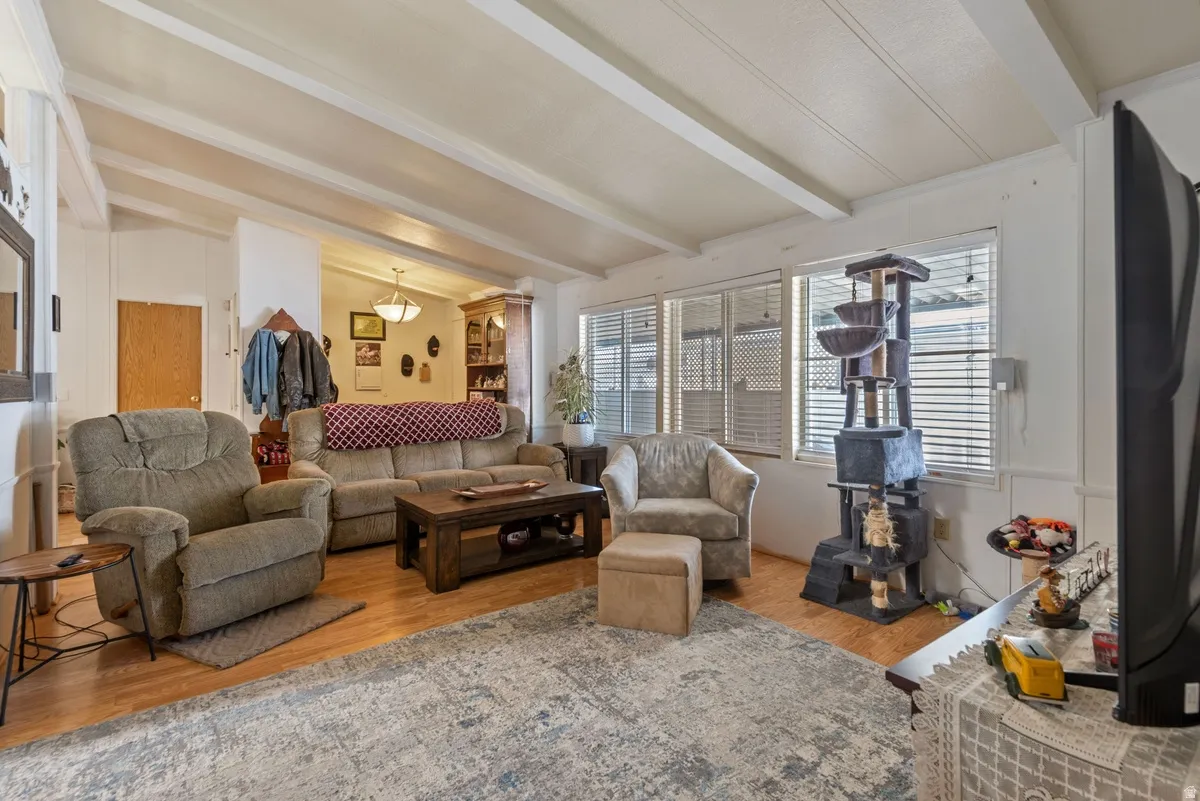 Spacious living area featuring wood-finish flooring, exposed beam ceiling, and ample natural light from multiple windows