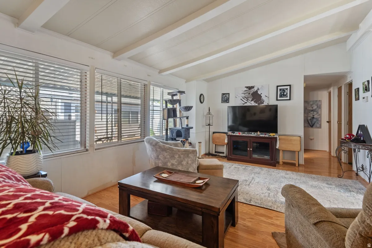 Living area featuring exposed ceiling beams, wood-finish flooring, a wall of windows with blinds, and white interior walls