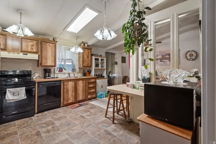 Kitchen featuring wood cabinetry, black appliances, a skylight, and durable tile flooring