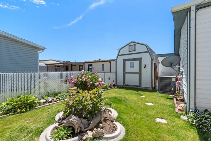 Manicured backyard featuring a chain-link fence, established landscaping, and a detached storage shed