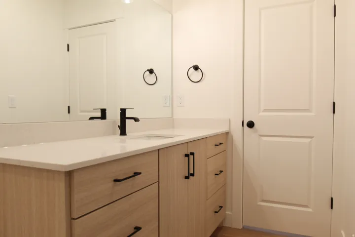 Bathroom vanity featuring a light wood-finish cabinet with matte black hardware, a light-toned countertop, and an undermount sink with a matte black faucet