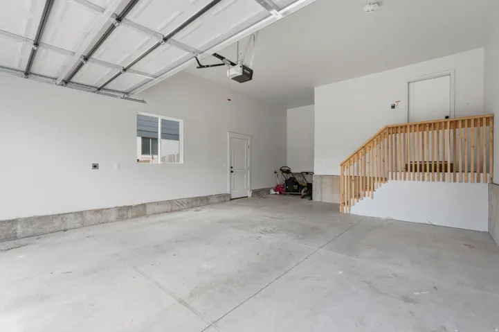 Spacious garage with concrete flooring, a single window, an interior access door, a garage door opener, and a wooden staircase
