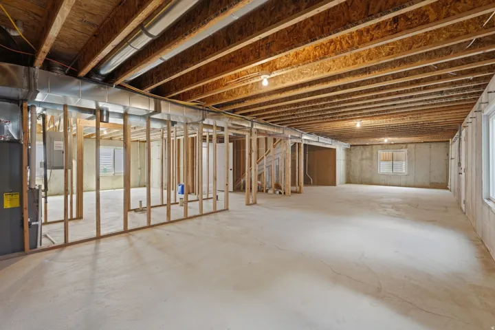 Unfinished lower level featuring exposed wood joists, concrete flooring, window wells, partial wood framing, and visible ductwork