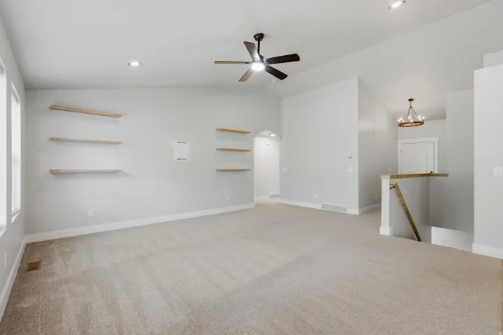 Carpeted living area featuring vaulted ceilings, recessed lighting, a ceiling fan, and built-in floating shelves