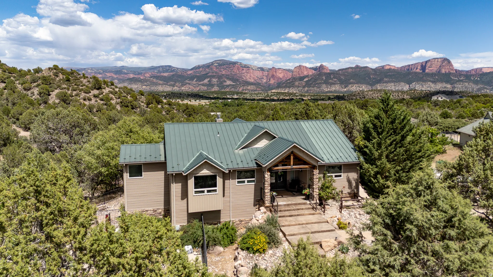 Contemporary residence with a green metal roof, a stone and wood beam entry, and multi-level exterior siding