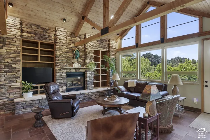 Spacious living area featuring a vaulted wood-plank ceiling with exposed beams, full-height stone accent walls, a built-in fireplace, and large windows