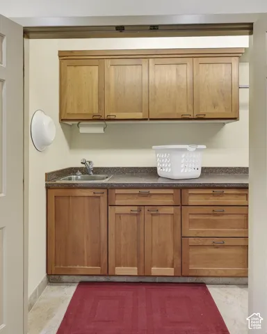 Utility room featuring wood cabinetry, stone-finish countertops, and a built-in sink