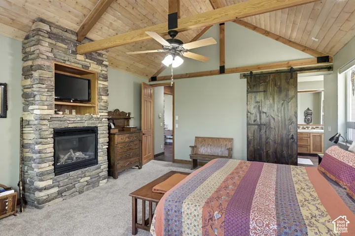 Vaulted wood-plank ceiling with exposed beams, featuring a stone-clad fireplace with built-in media niche, ceiling fan, and a rustic barn door entryway