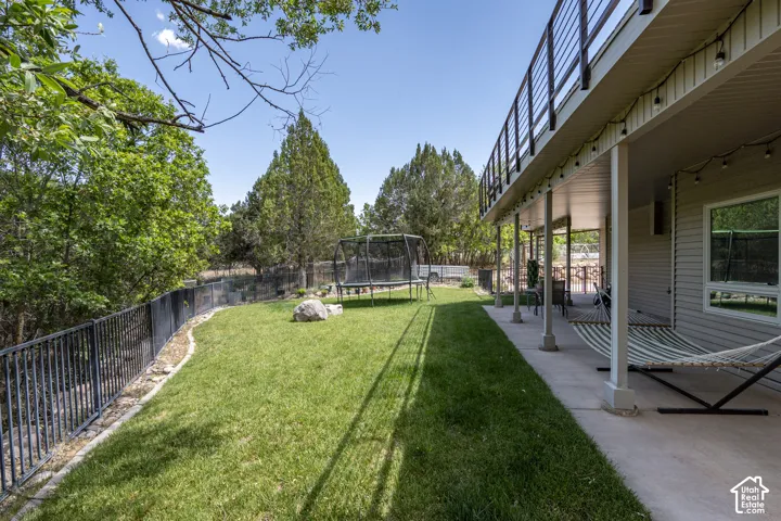 Spacious backyard featuring a manicured lawn, a black metal fence, and mature trees