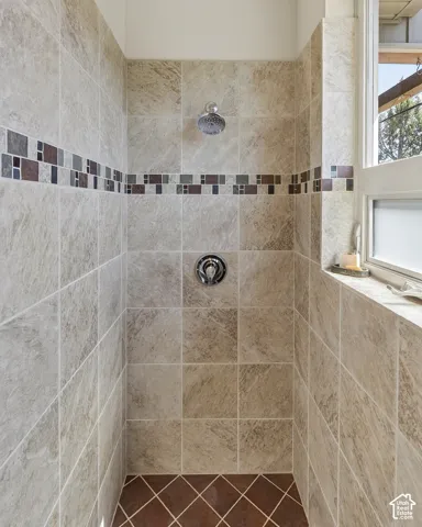 Tiled shower enclosure featuring a multi-toned decorative mosaic accent band, a chrome shower head, and a matching chrome temperature control fixture