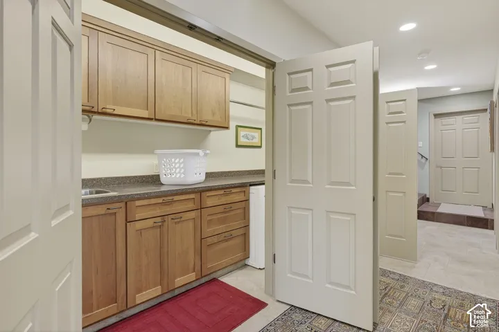 Laundry area featuring natural wood cabinetry, stone-look countertop with integrated sink, and overhead storage