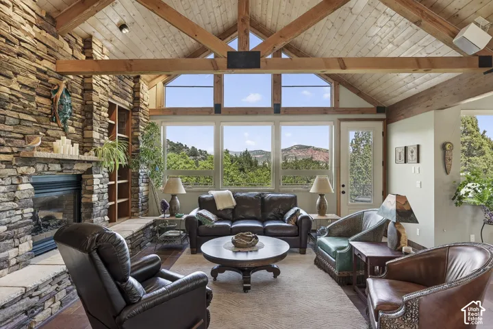 Vaulted wood-plank ceilings with exposed beams, a floor-to-ceiling stone fireplace, built-in shelving, expansive windows, and wood-finish flooring