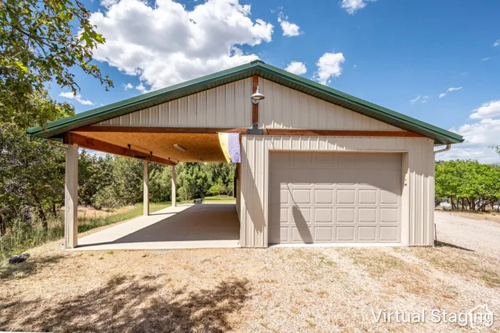 Detached outbuilding featuring a metal roof, light-toned siding, an attached single-car garage, and a covered carport with concrete flooring and exposed wood beams