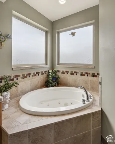Corner jetted tub set within a tiled surround featuring a mosaic accent band