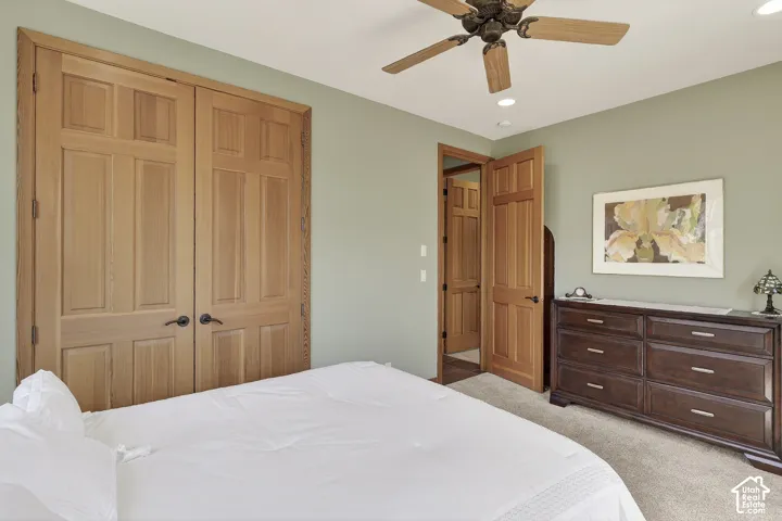 Bedroom with light green walls and neutral carpeting, featuring natural wood-finish paneled doors, recessed lighting, and a ceiling fan