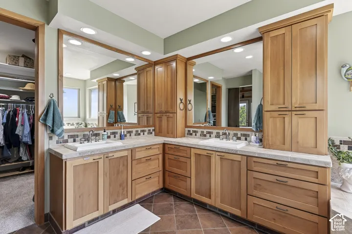 Bathroom featuring a dual vanity with light-tone wood cabinetry, recessed lighting, integrated sinks, and patterned tile backsplash