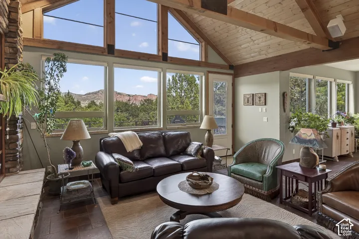 Vaulted ceiling with exposed wood beams and planking, floor-to-ceiling windows, stone fireplace surround, tiled flooring, and a glass-paneled door