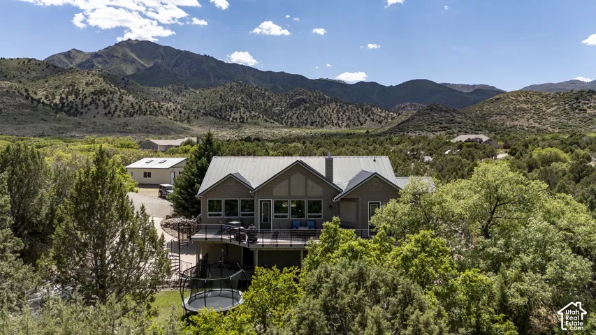 Modern mountain residence featuring a multi-level deck, a metal roof, and a backdrop of mountainous terrain