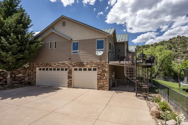 Exterior featuring stacked stone accents, two garage doors, and a spiral staircase leading to an elevated deck