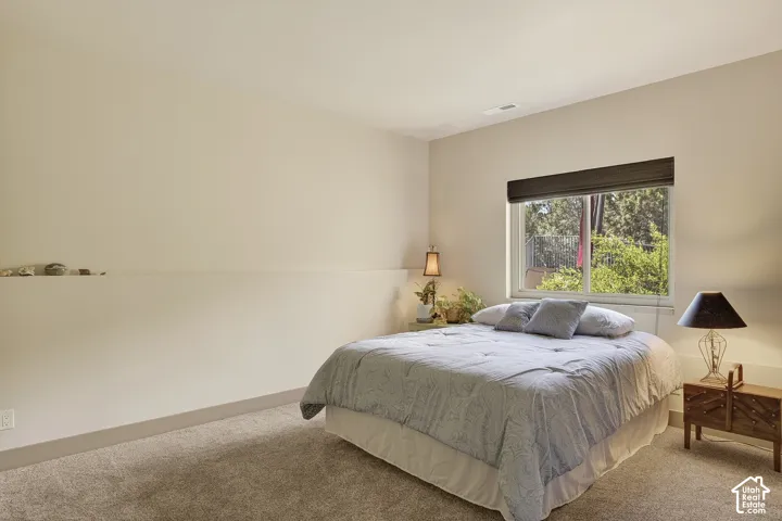 Carpeted room featuring a large window with a dark roller shade, a built-in wall shelf, light-toned walls, and white trim
