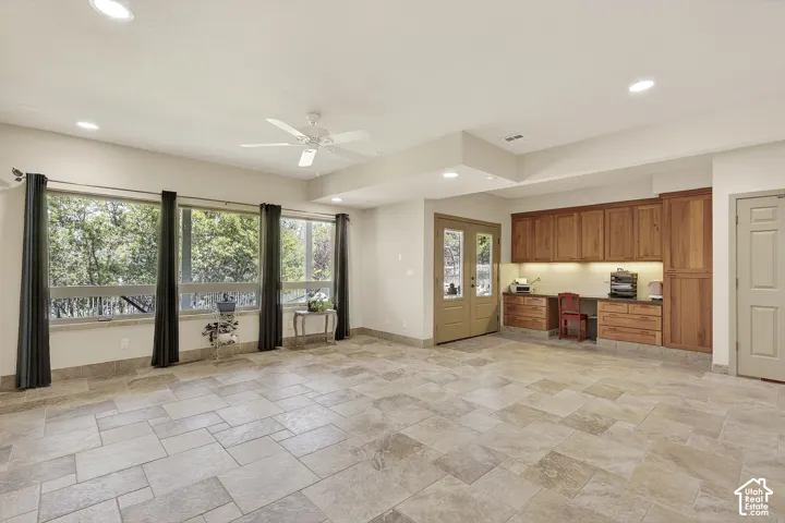 Spacious room with large-format tile flooring, a wall of windows, recessed lighting, and a built-in wood cabinetry system with desk space