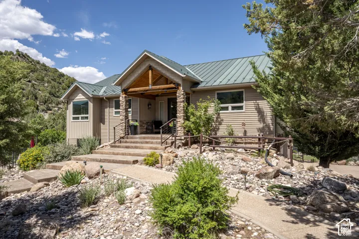 Front exterior featuring stacked stone columns, a covered entry with timber accents, and a metal roof