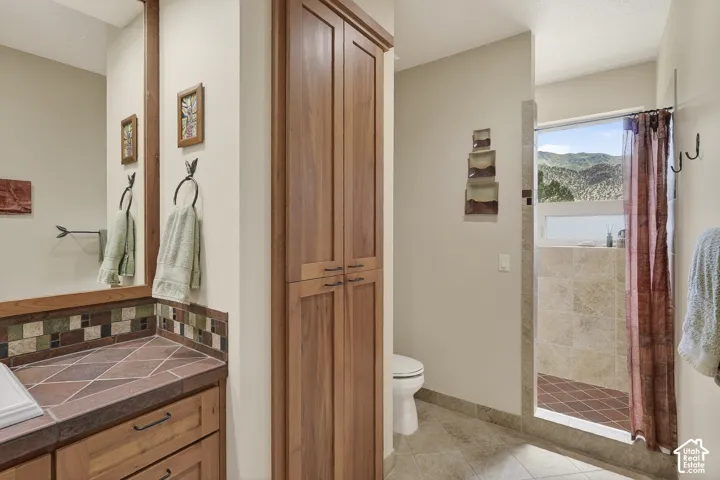 Bathroom featuring a walk-in shower with tile surround, a built-in storage cabinet, a vanity with a tile countertop and backsplash, and a large mirror