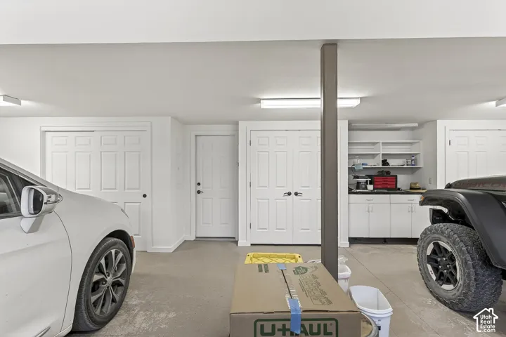 Spacious garage with multiple overhead light fixtures, built-in storage shelving, white cabinetry, and two sets of double-panel closet doors