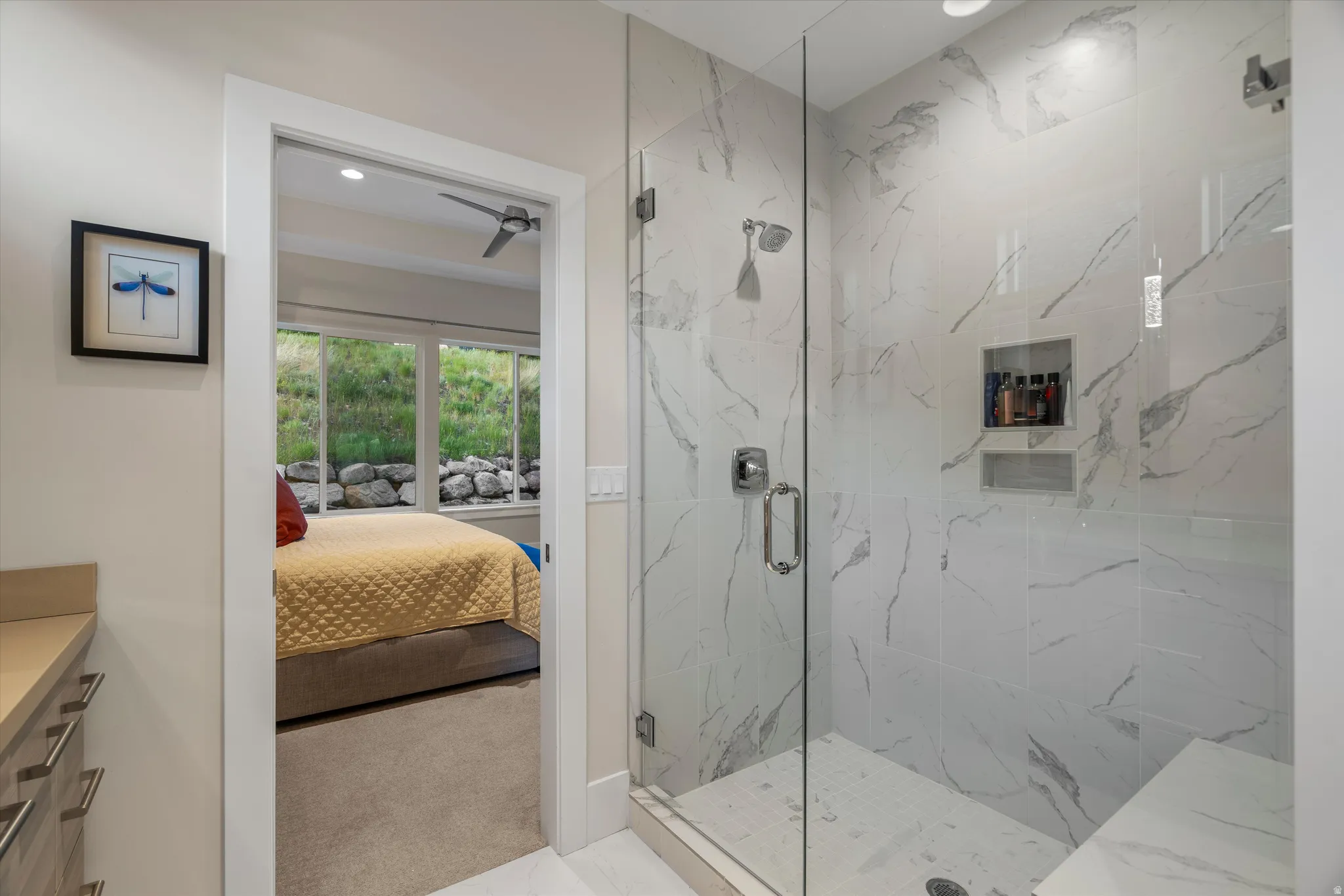 Glass-enclosed shower featuring large format marbled tile, a built-in bench, and dual recessed niches