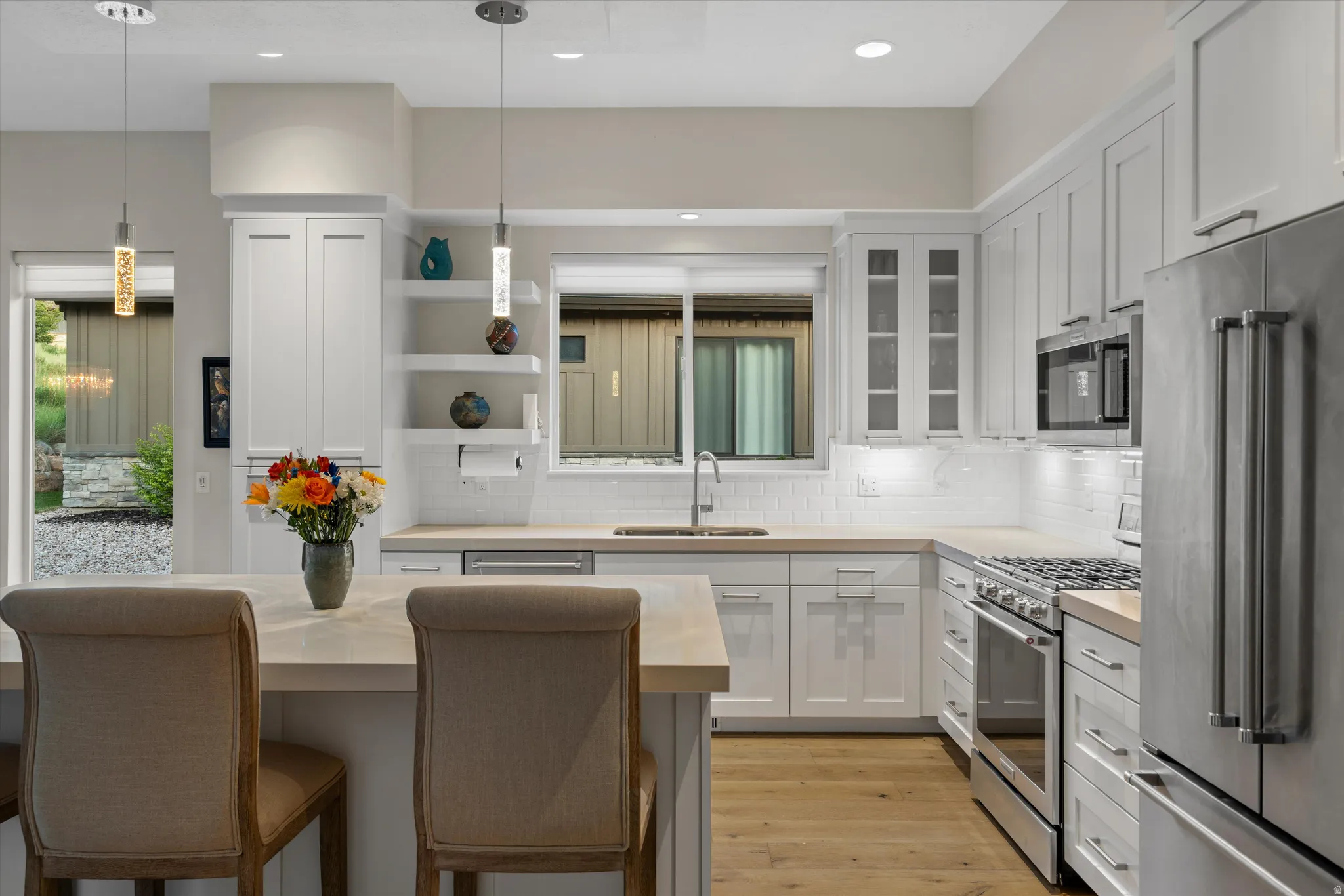 Modern kitchen featuring white shaker cabinetry, stainless steel appliances, light wood-finish flooring, a white subway tile backsplash, and a central island with pendant lighting