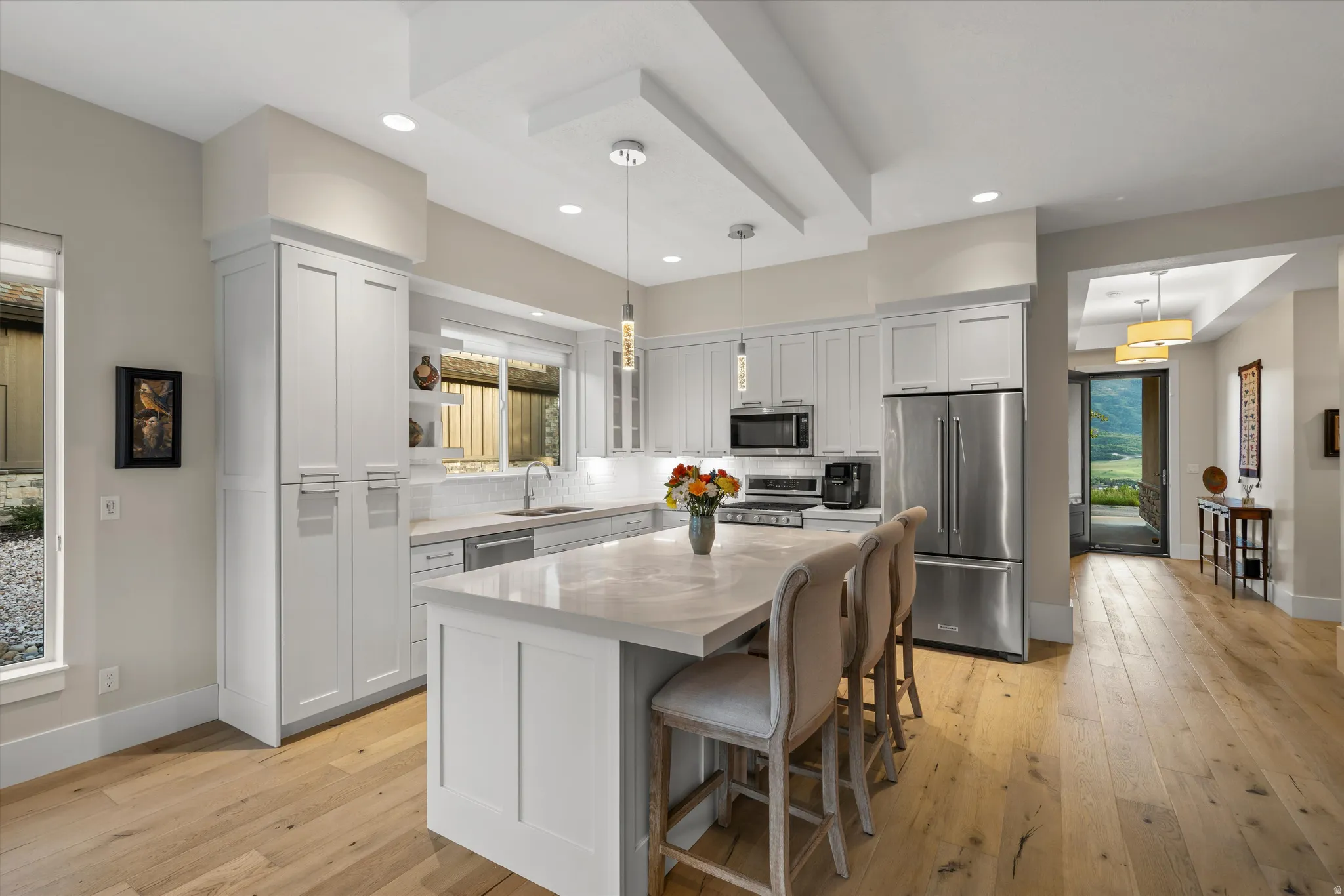 Modern kitchen featuring white shaker cabinetry, stainless steel appliances, a large center island with seating, recessed lighting, and wood-finish flooring