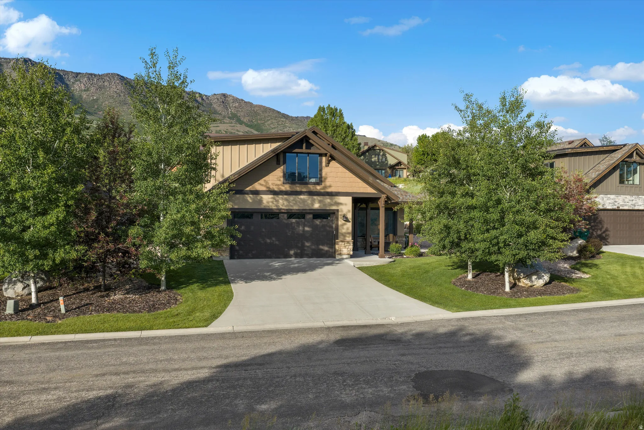 Craftsman-style home featuring a two-car garage, concrete driveway, and natural wood and stone facade