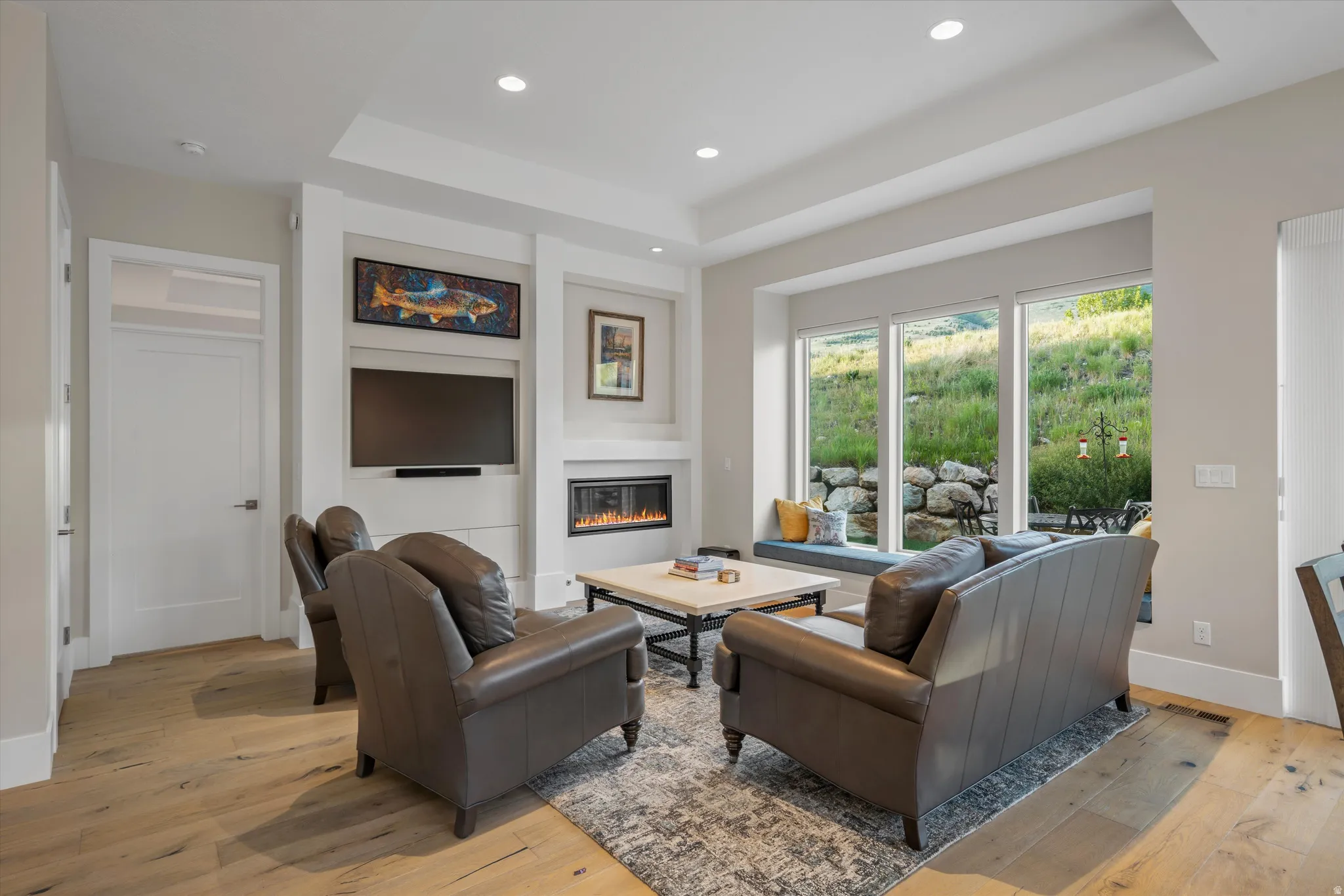 Living area featuring wide plank wood-finish flooring, a recessed gas fireplace, built-in media center, and a window seat with exterior landscaping