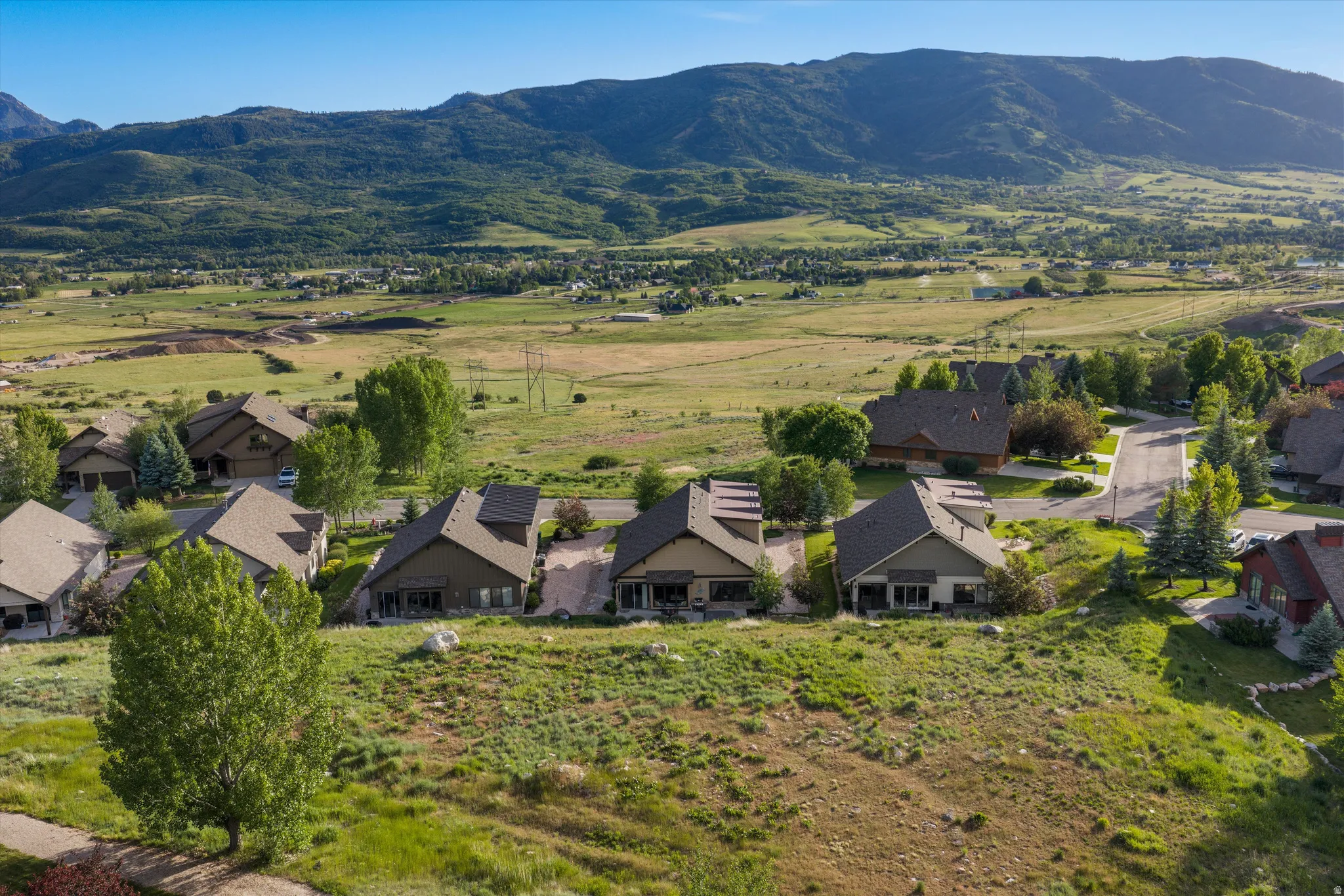 Expansive mountain and valley scenery provides a backdrop for residences with sloped roofs and mature landscaping