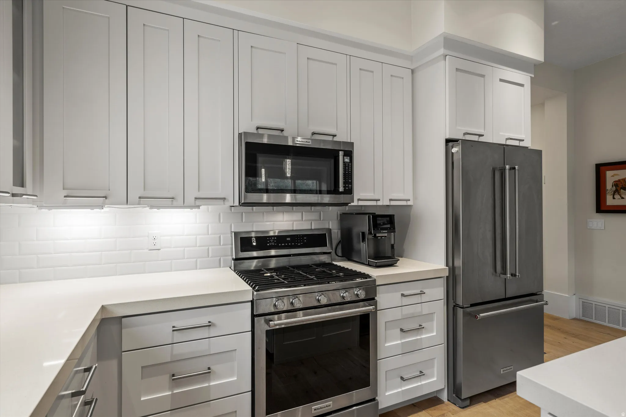 Kitchen featuring white shaker-style cabinetry, stainless steel appliances, a white subway tile backsplash, and light-colored countertops