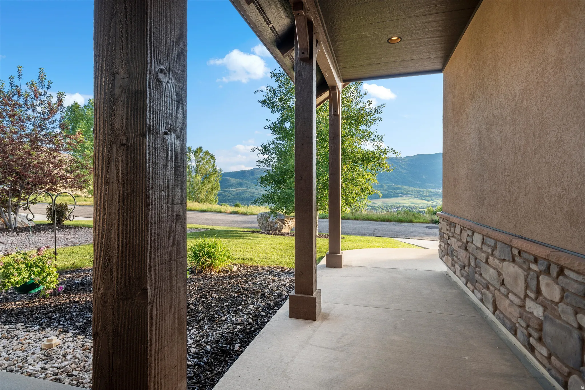 Covered porch entry featuring exposed wood-finish columns and a stucco exterior with a natural stone wainscot