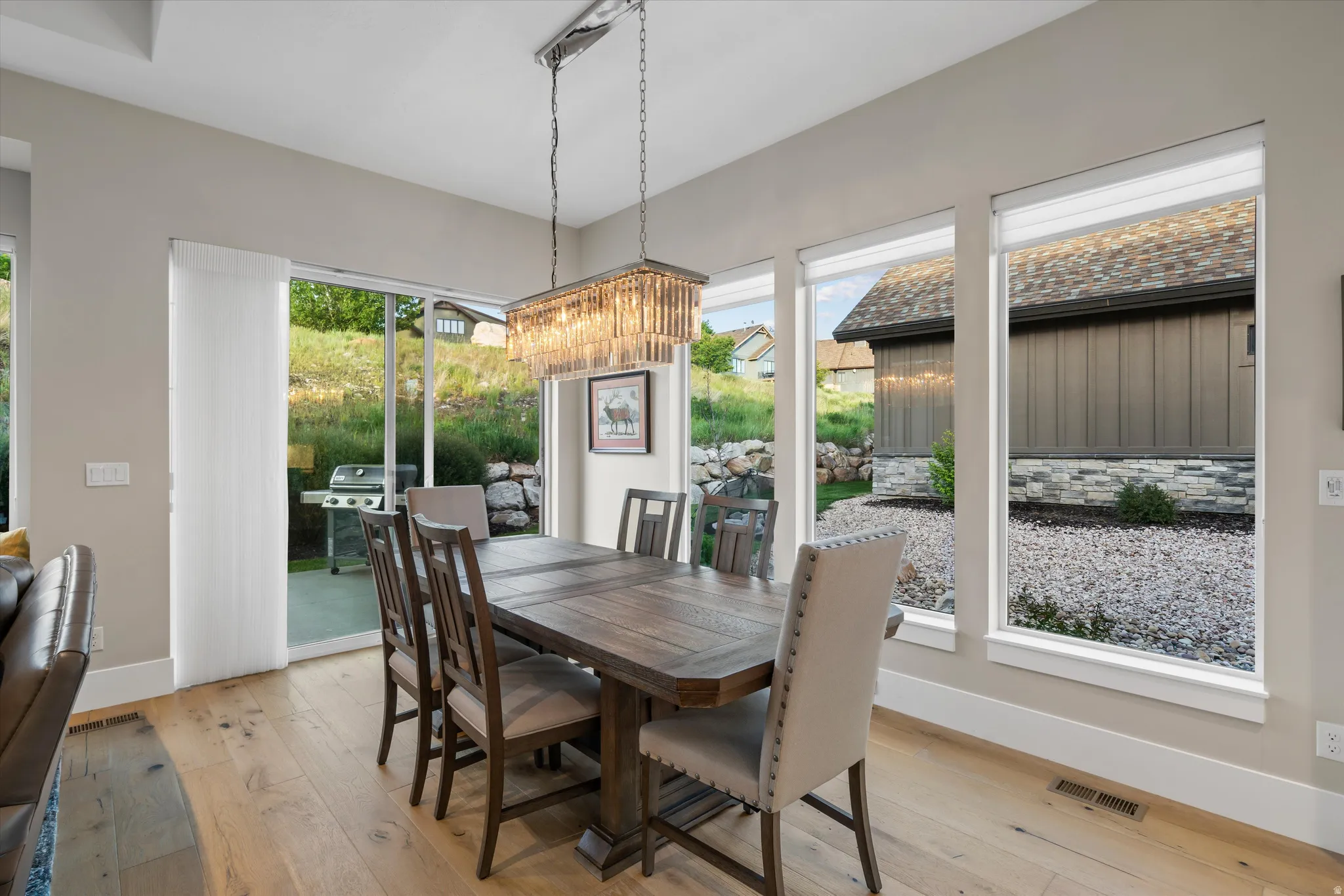Dining area with wood-finish flooring, featuring a rectangular chandelier and expansive window array