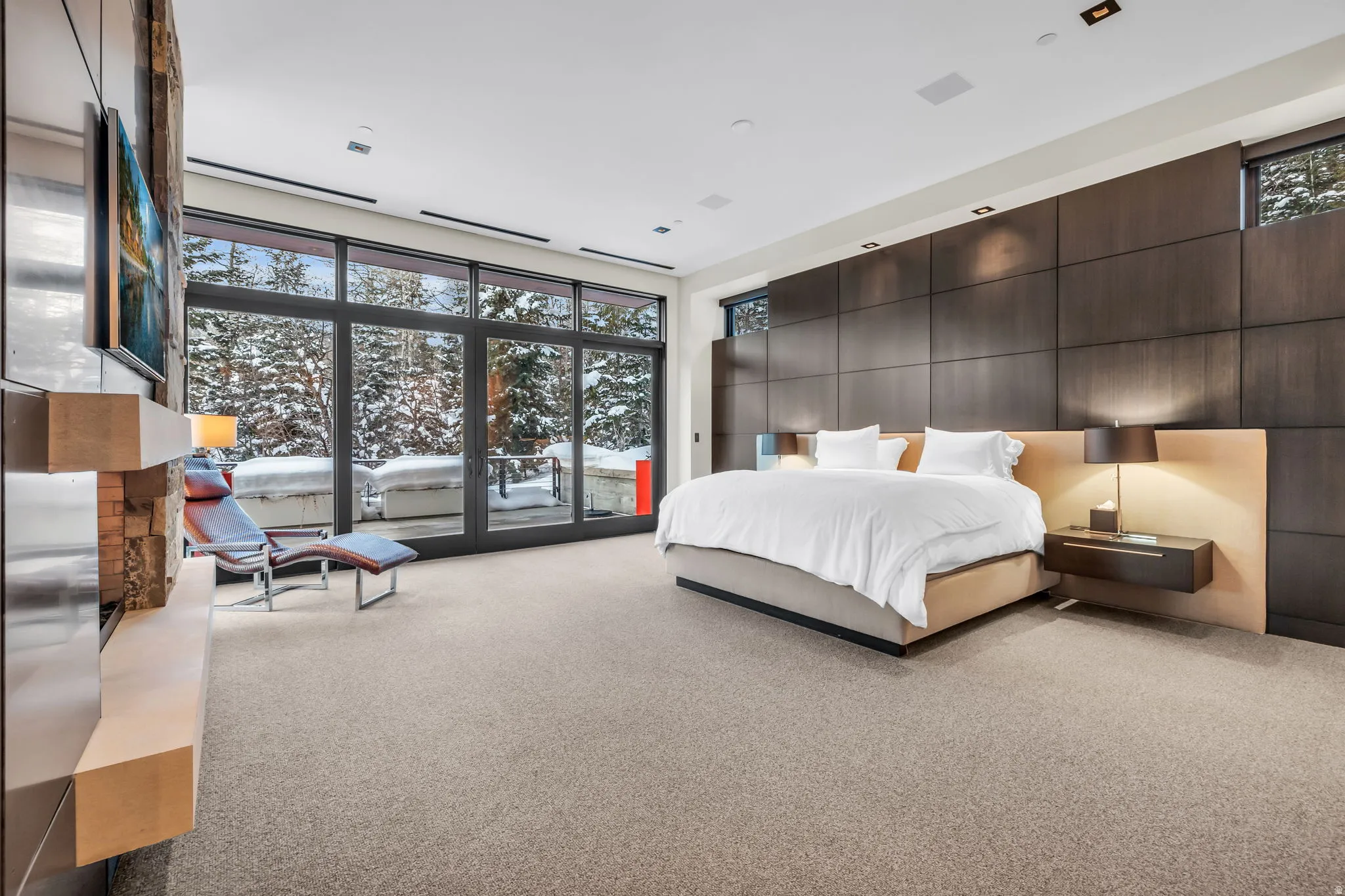 Floor-to-ceiling windows with dark frames, a built-in stone fireplace feature, dark wood paneling, and a light-toned carpet
