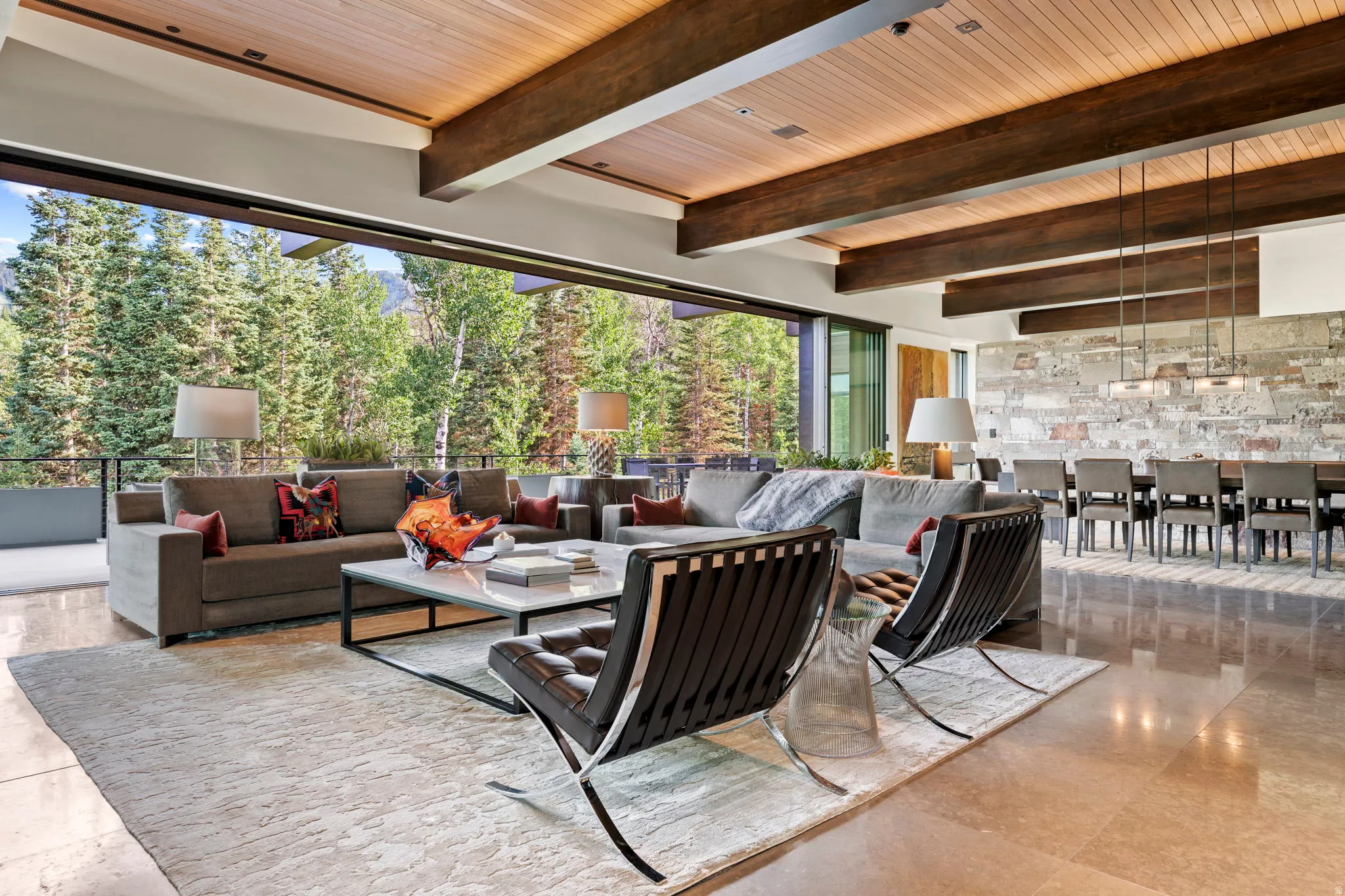 Expansive living area featuring a wood-panel ceiling with exposed beams, polished stone flooring, and a floor-to-ceiling retractable glass wall
