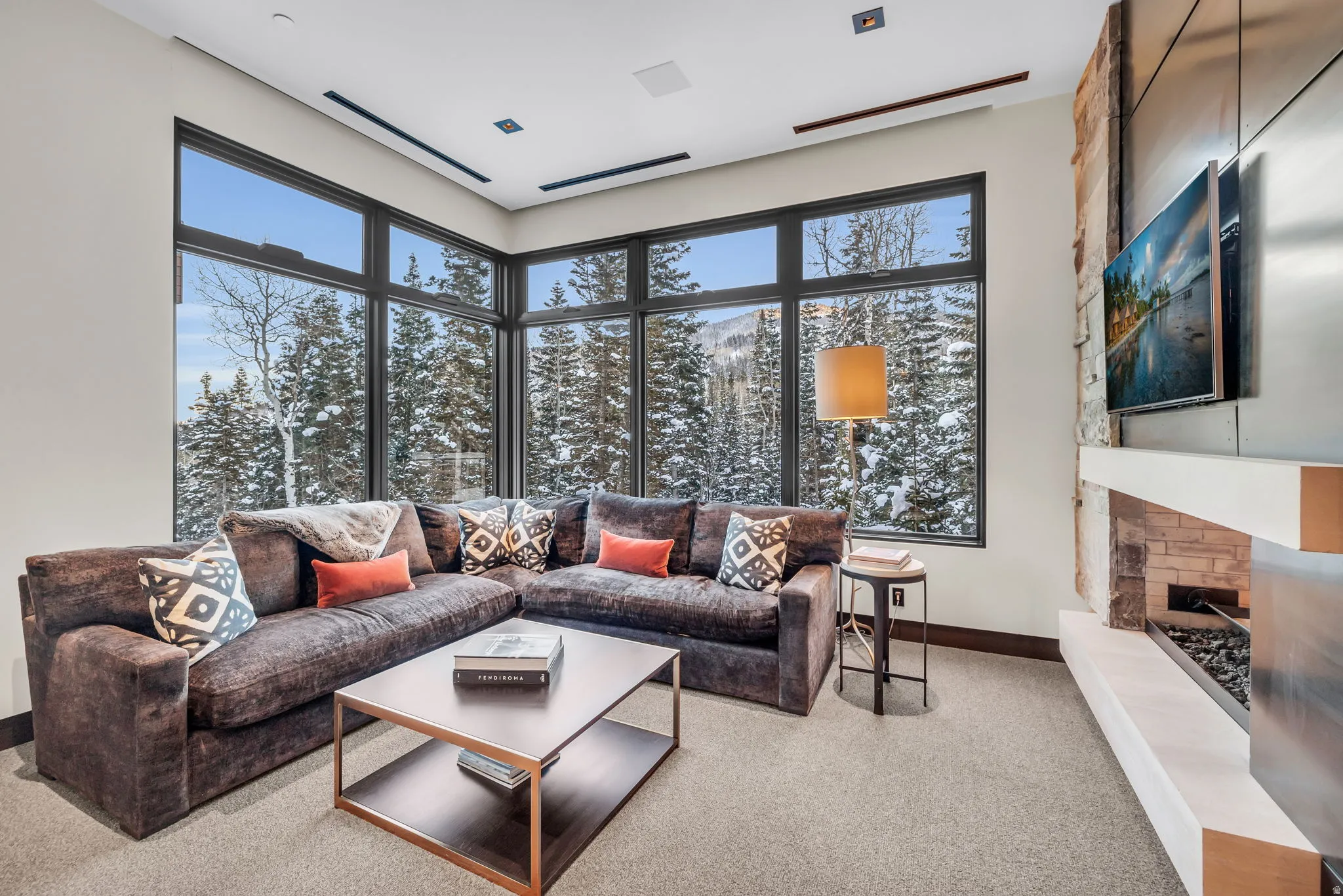Spacious living area featuring extensive window walls, a linear fireplace with stone surround, a floating mantel, and high ceilings with recessed lighting