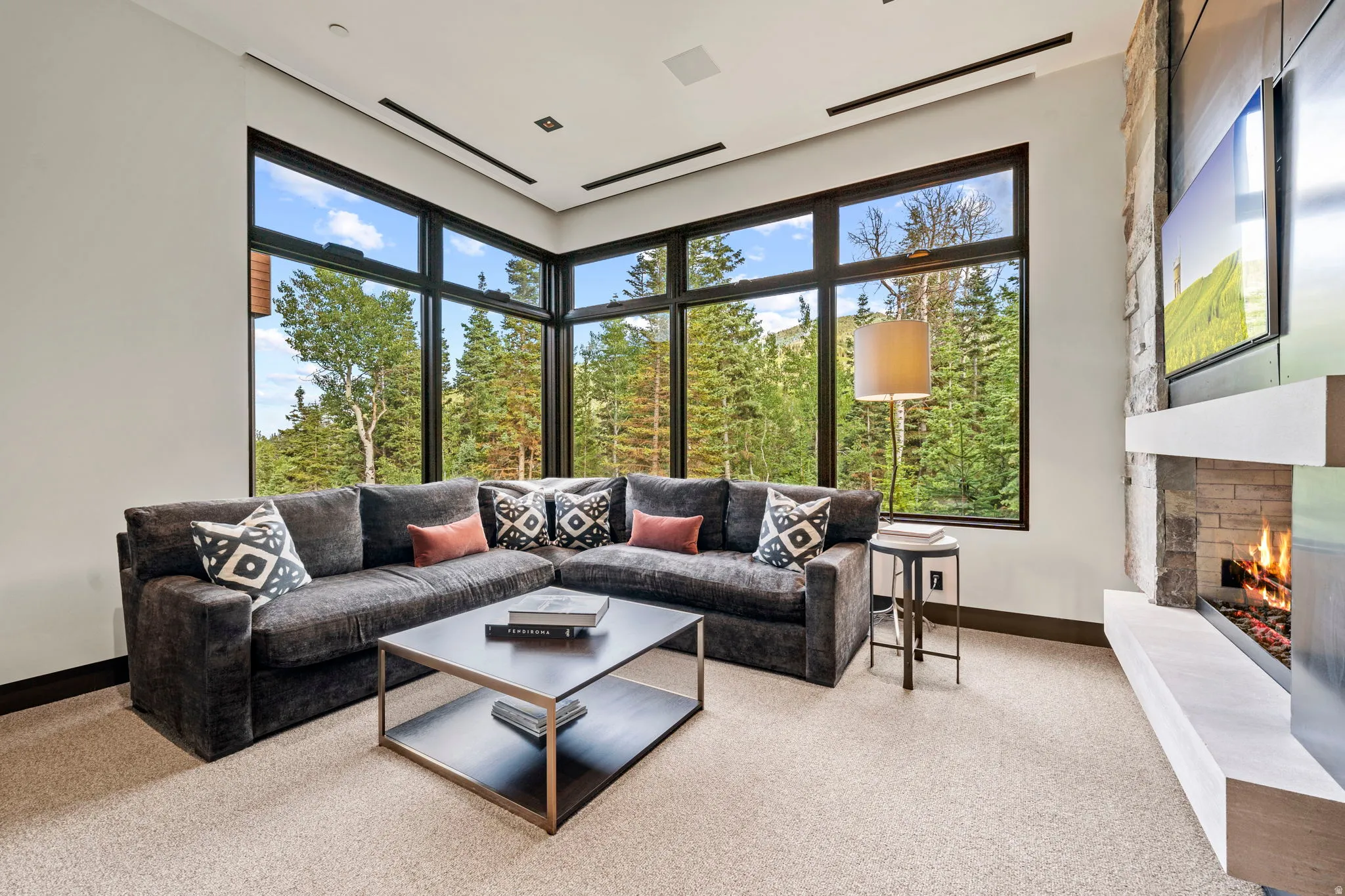 Floor-to-ceiling windows, a stone-clad fireplace with a hearth, recessed ceiling lighting, and dark trim details