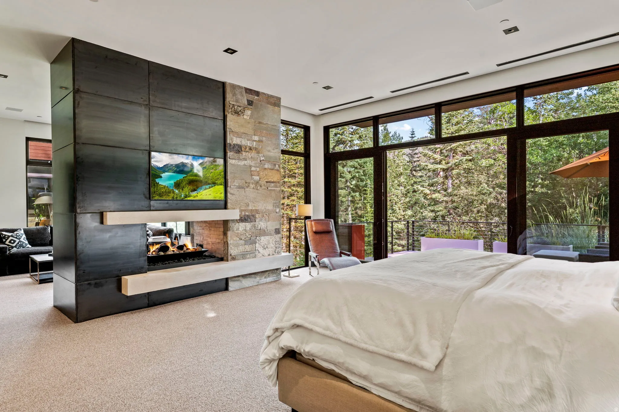 Floor-to-ceiling windows with expansive glass, a stone and metal fireplace feature, gas fireplace, light-toned carpet flooring, and a recessed ceiling
