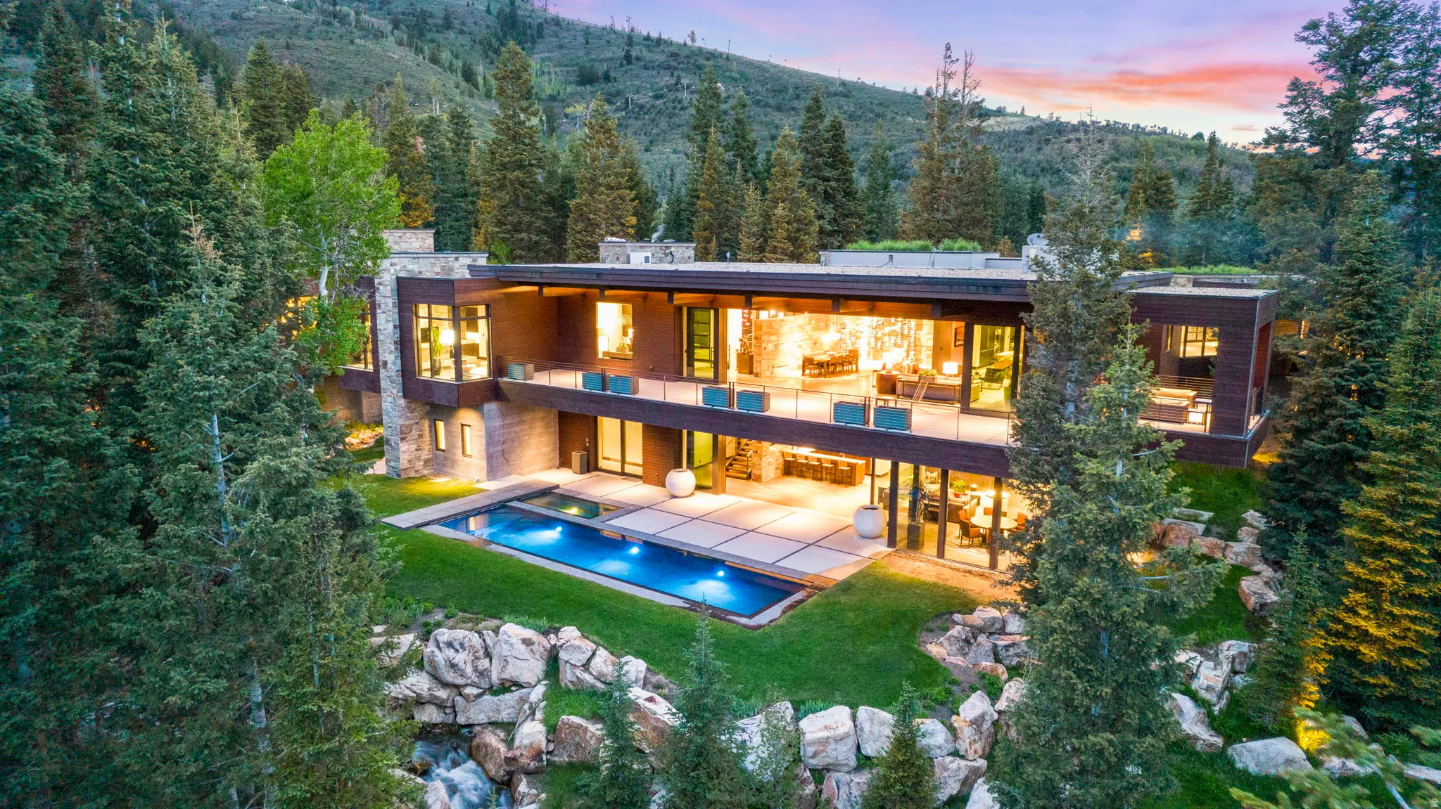 Modern architectural residence featuring extensive glass facades, multiple outdoor balconies, a rectangular swimming pool, and a structured outdoor patio space