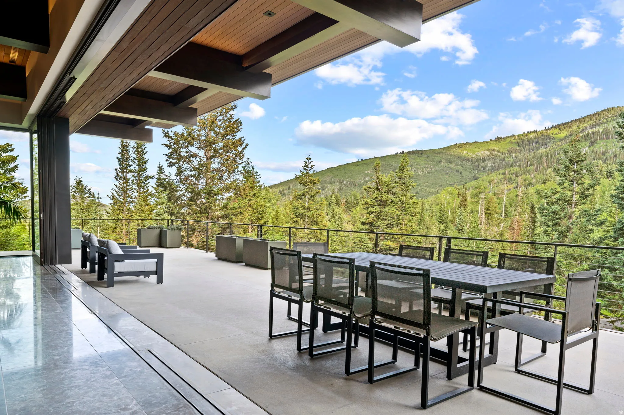 Expansive outdoor patio featuring a wood-panel ceiling, concrete flooring, and a contemporary metal railing