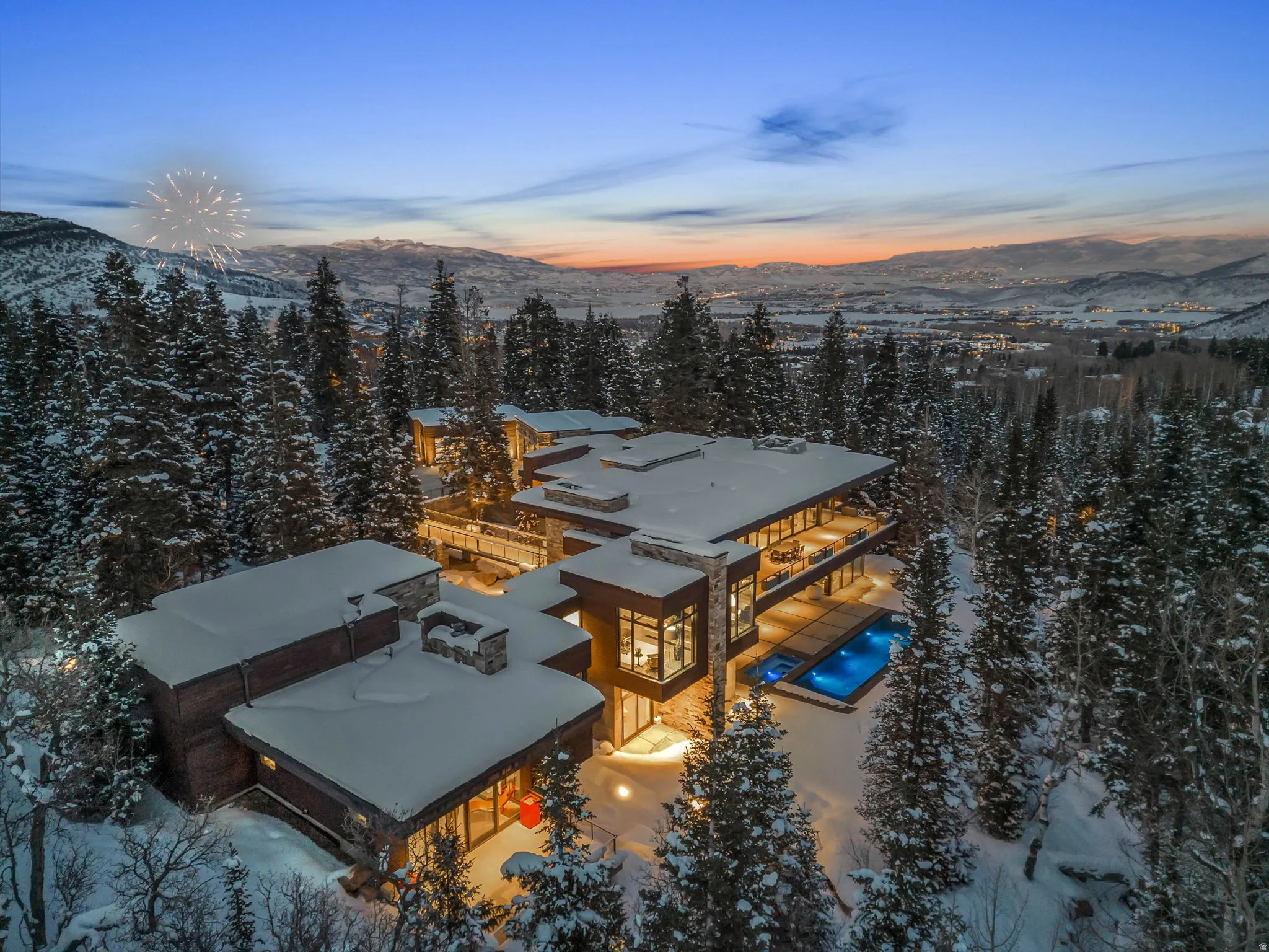 Expansive architectural residence featuring multiple outdoor terraces, large format windows, a stone exterior, and an illuminated outdoor pool