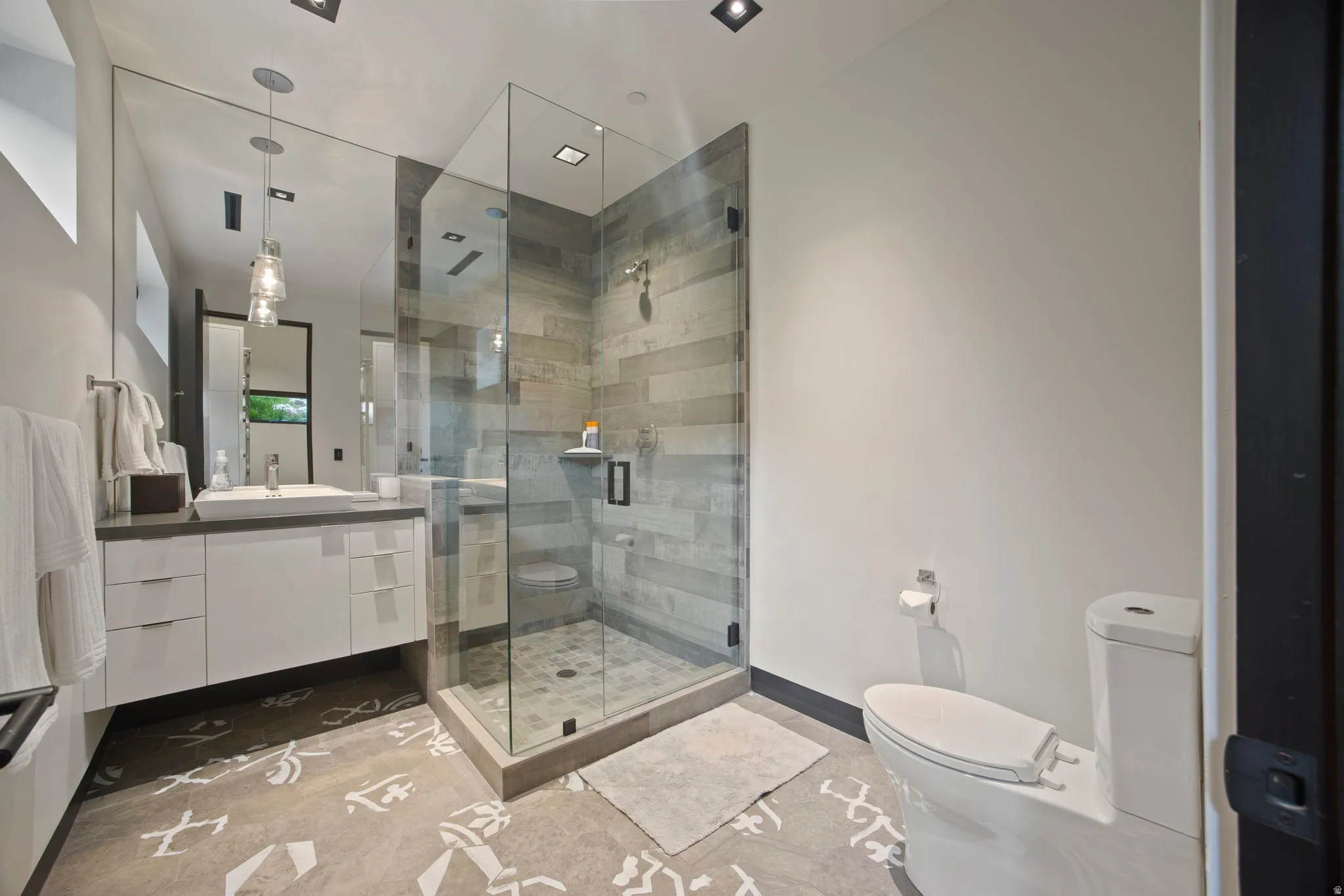Modern bathroom featuring a glass-enclosed shower with horizontal tile, a floating vanity with a vessel sink, and patterned floor tile