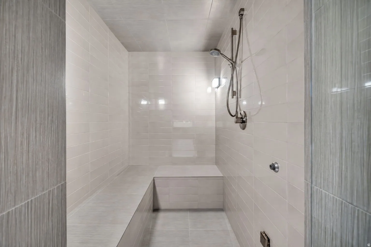 Expansive walk-in shower featuring light-toned subway tile, a built-in bench, brushed nickel shower fixtures, and integrated wall lighting