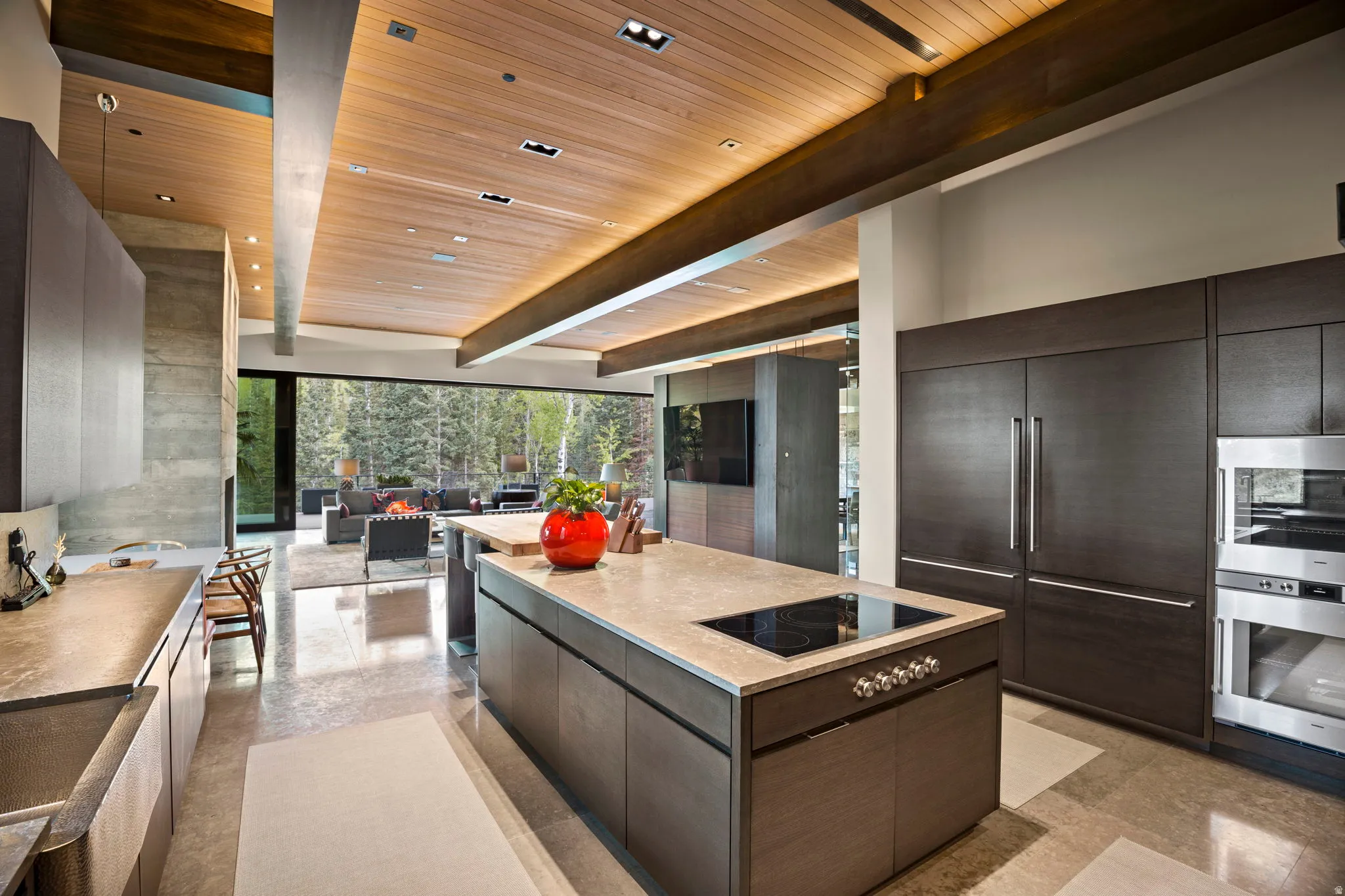 Modern kitchen featuring dark wood-finish cabinetry, integrated stainless steel appliances, a large center island with an induction cooktop, and light-toned countertops